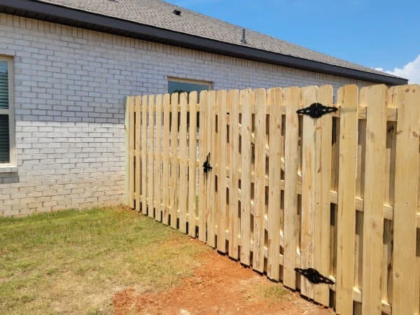 Shadowbox wood fence and walk gate with black hardware beside a brick home